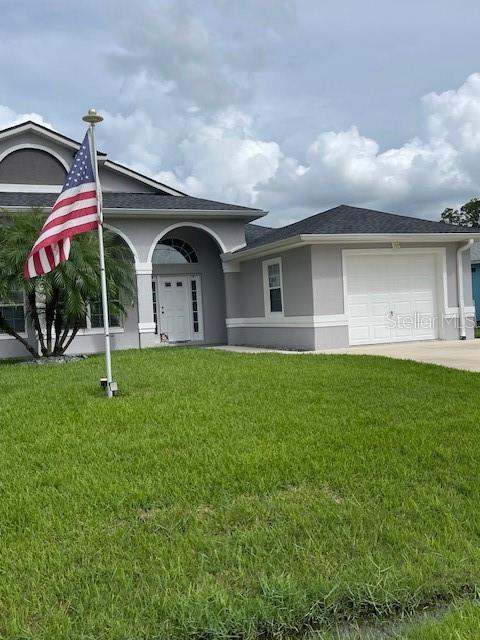 A single-story gray house with a white garage door and an American flag in the yard — 23 RIDLEY LANE UNIT B, PALM COAST, FL