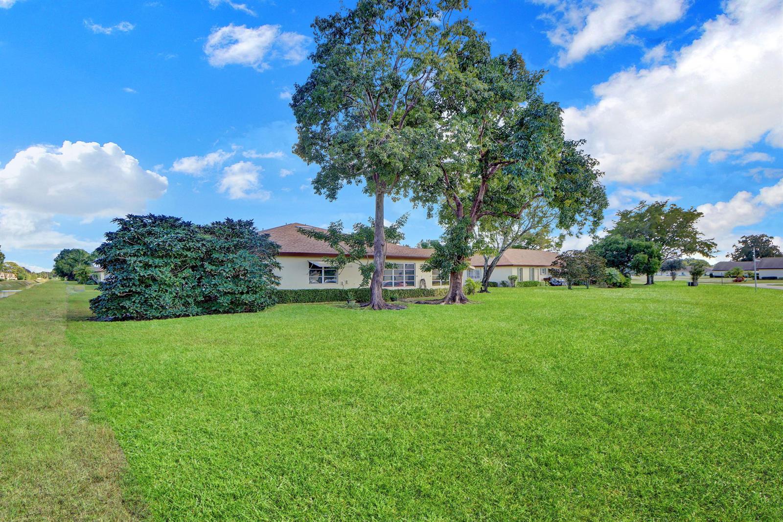A single-story house with a large lawn, mature trees, and a dense shrubbery hedge — 14050 Nesting Way # B, Delray Beach FL 33484, DELRAY BEACH, FL