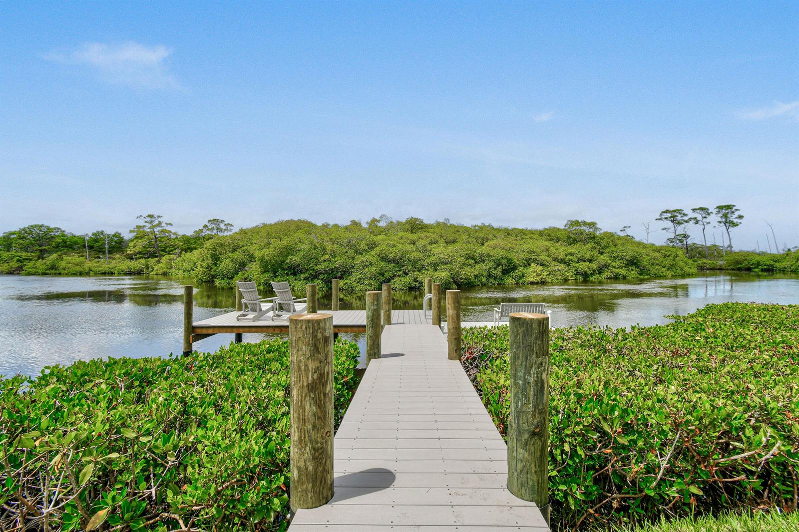 A wooden dock with chairs extends over a calm waterway surrounded by lush green mangroves — 10541 SE Le Parc, Jupiter FL 33469, JUPITER, FL