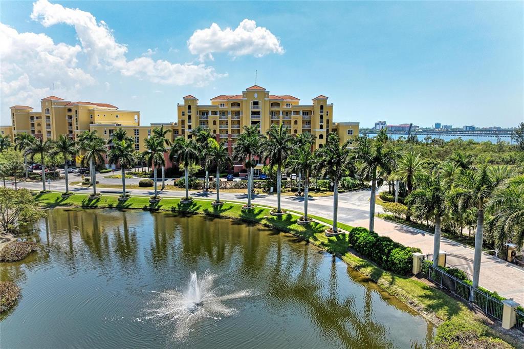 An aerial view of a yellow multi-story apartment building with a fountain in a pond — 611 RIVIERA DUNES WAY UNIT 403, PALMETTO, FL