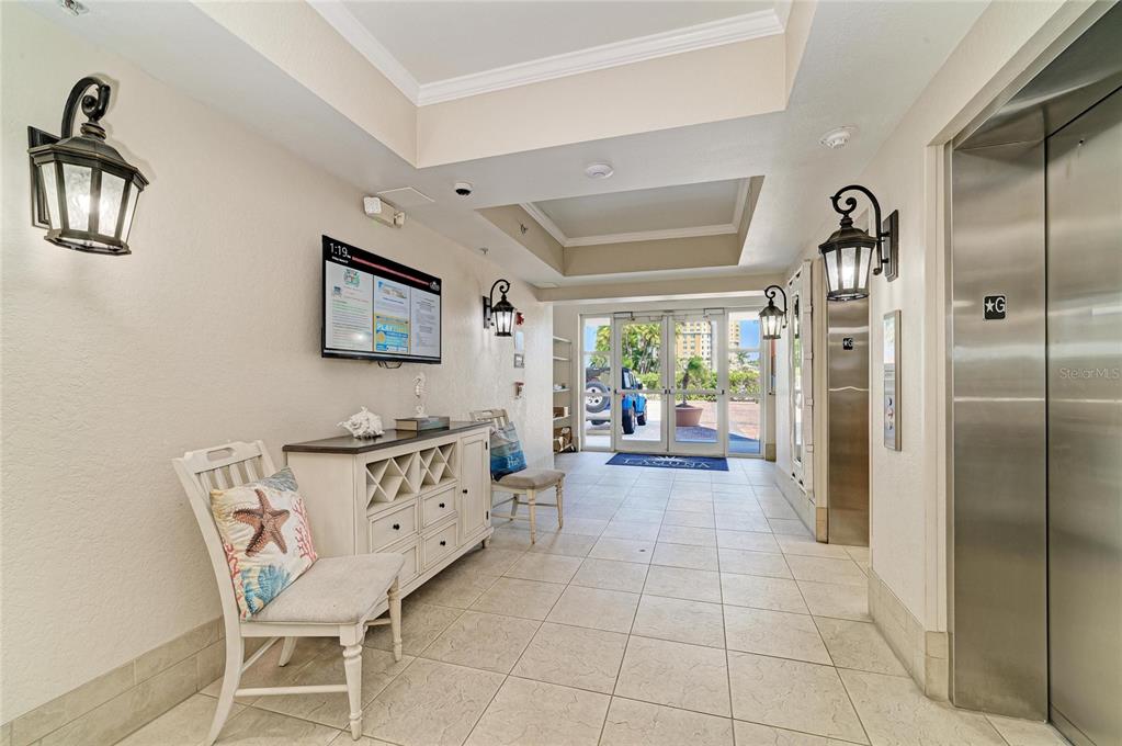 A lobby area features tile flooring, a white console table, a chair, and an elevator — 611 RIVIERA DUNES WAY UNIT 403, PALMETTO, FL