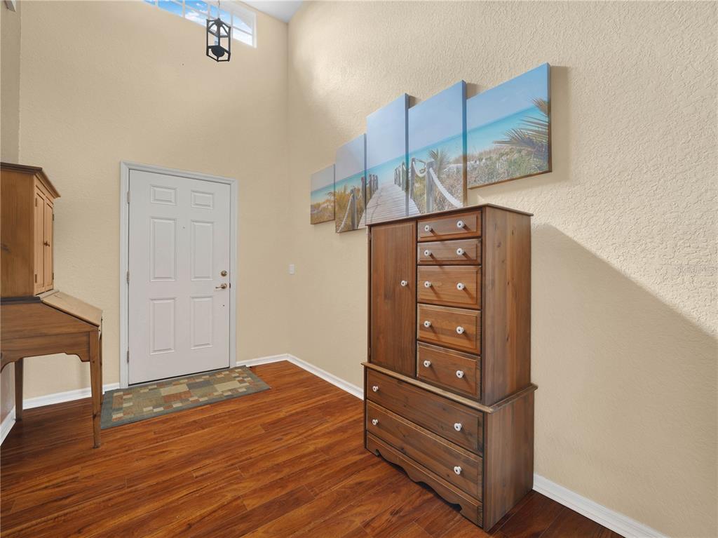 An entryway features wood flooring, a white door, a tall wooden dresser, and beach artwork — 4144 ABERDEEN LANE, LAKE WALES, FL