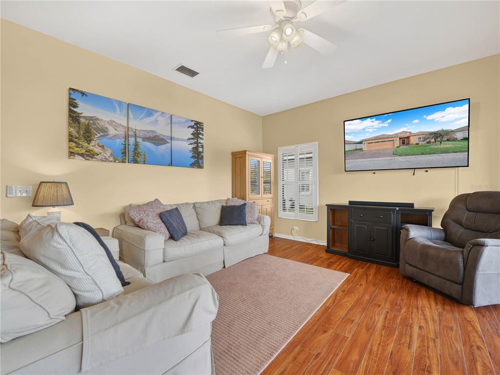A living room features a beige sofa, a gray recliner, a television, and wood flooring — 4144 ABERDEEN LANE, LAKE WALES, FL