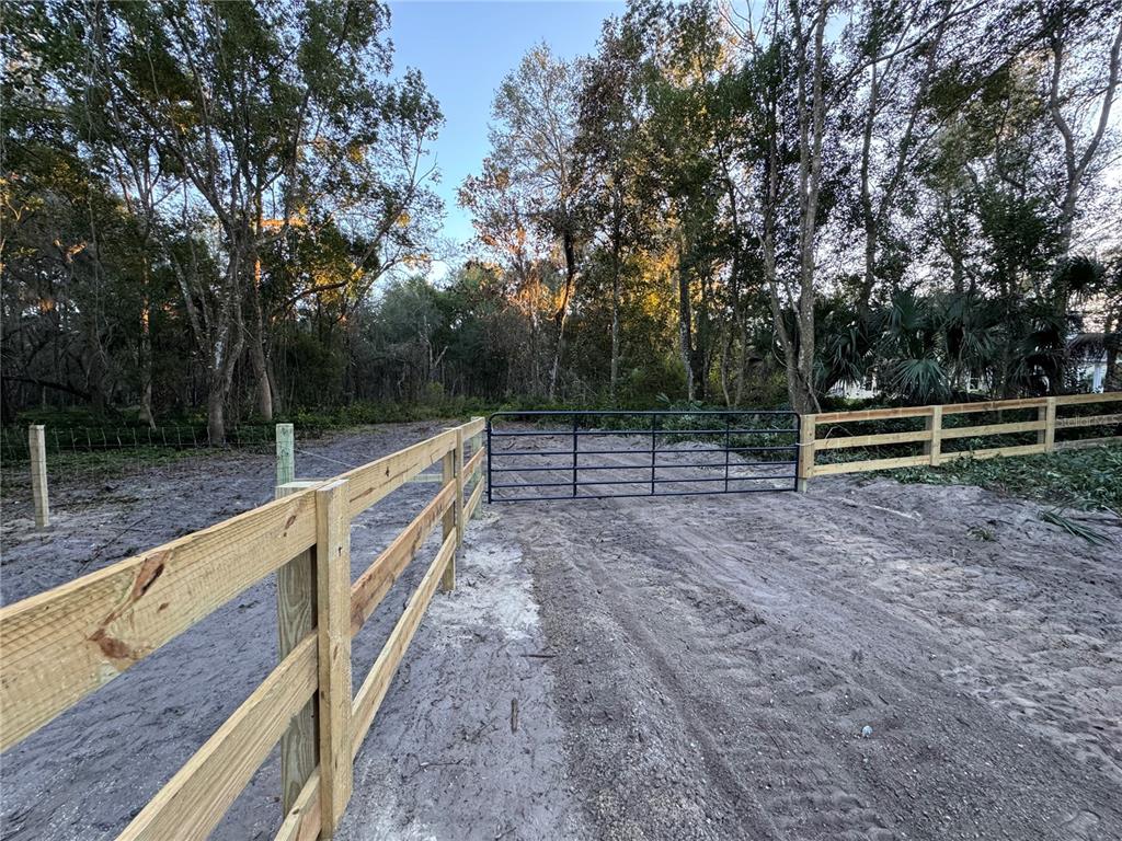 A metal gate sits between sections of a wooden fence on a sandy dirt path — W OHIO AVENUE, LAKE HELEN, FL