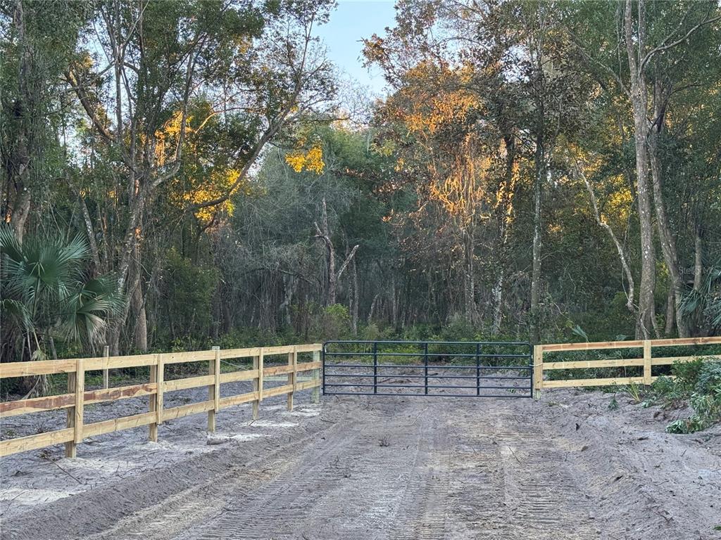 A metal gate connects sections of a wooden fence at the entrance to a wooded lot — W OHIO AVENUE, LAKE HELEN, FL