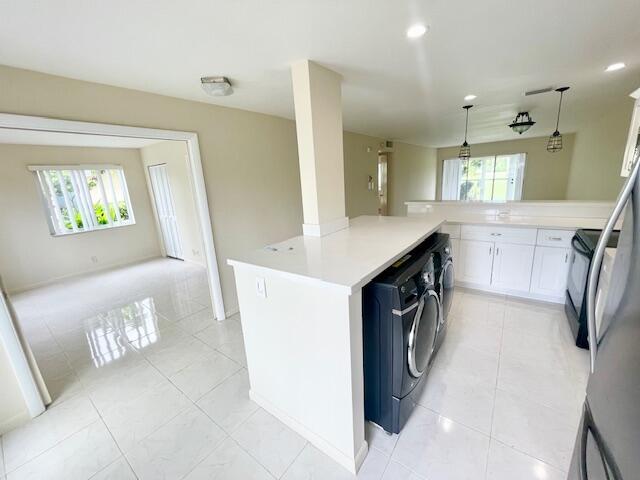 A kitchen with white cabinets, a central island, and a washer-dryer unit on tile floors — 13757 Flora Place # A, Delray Beach FL 33484, DELRAY BEACH, FL