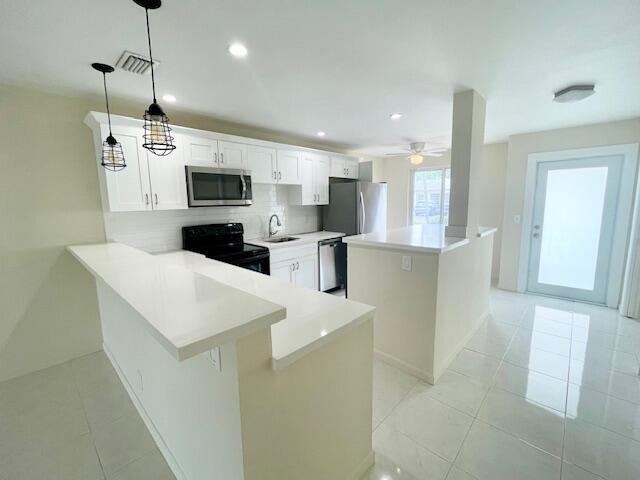 A modern kitchen features white cabinetry, quartz countertops, stainless steel appliances, and tile flooring — 13757 Flora Place # A, Delray Beach FL 33484, DELRAY BEACH, FL