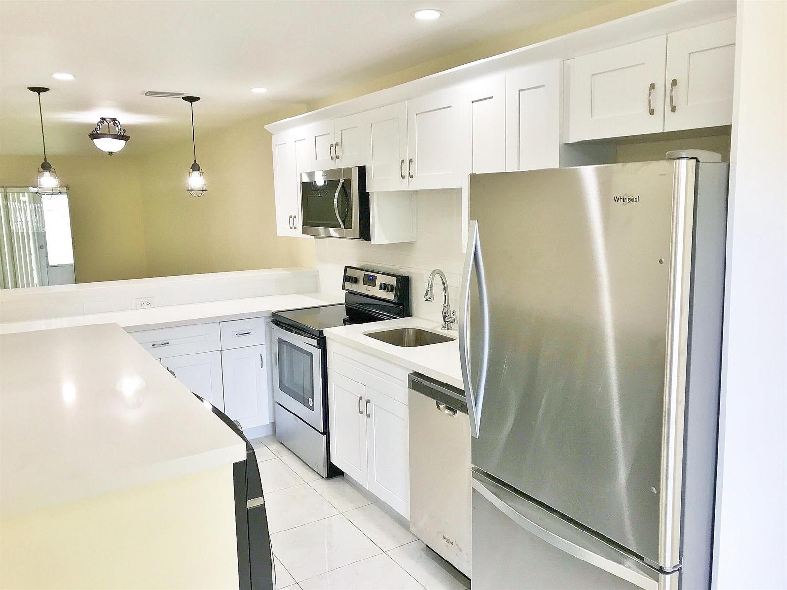 A modern kitchen featuring white cabinets, stainless steel appliances, and white countertops — 13757 Flora Place # A, Delray Beach FL 33484, DELRAY BEACH, FL
