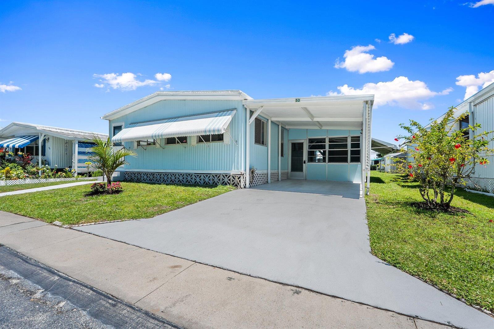 A light blue mobile home features a concrete driveway, a carport, and a white awning — 4800 SE Federal Highway # 53, Stuart FL 34997, STUART, FL