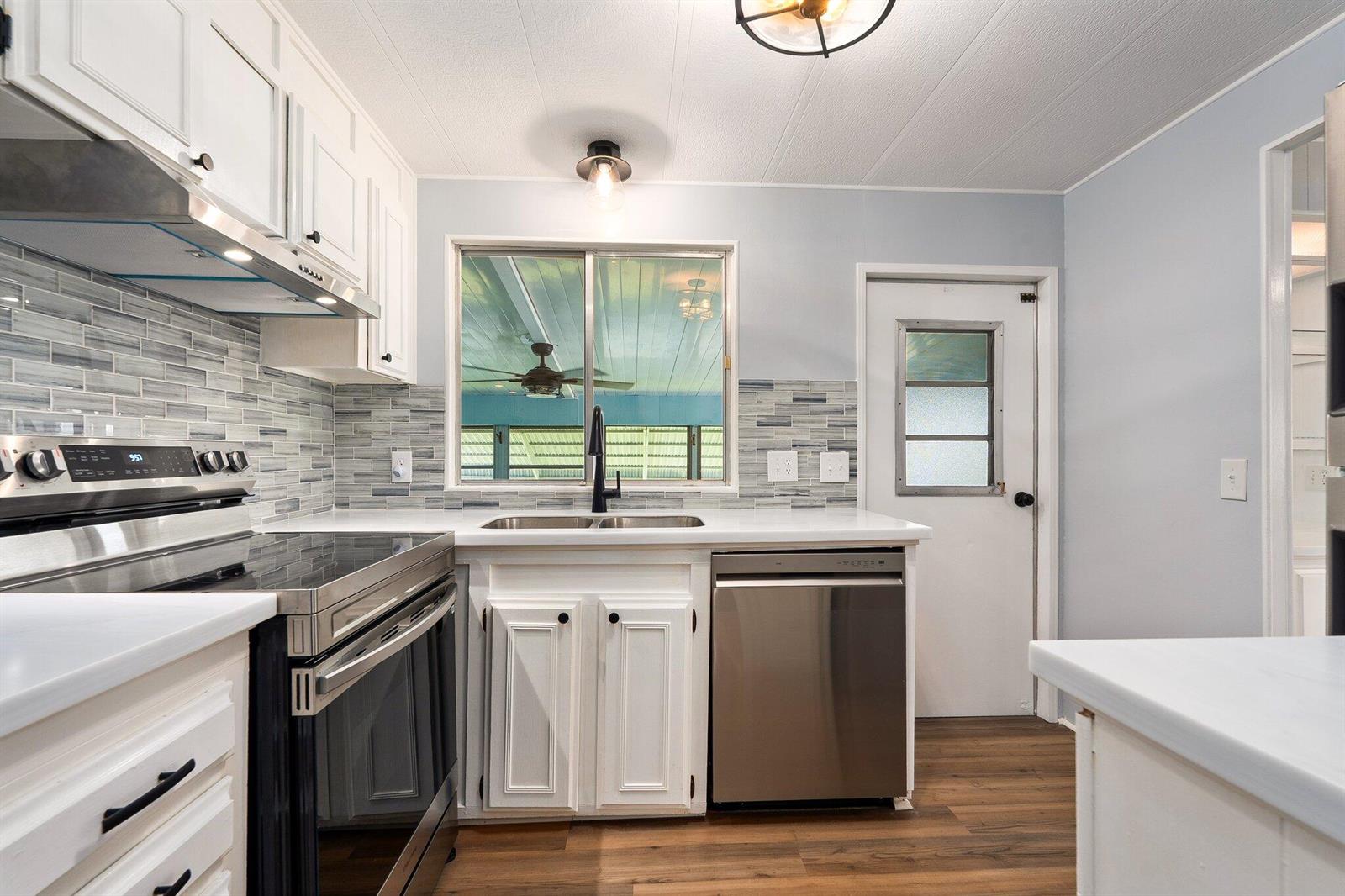 A kitchen with white cabinets, stainless steel appliances, a tiled backsplash, and wood-look flooring — 4800 SE Federal Highway # 53, Stuart FL 34997, STUART, FL