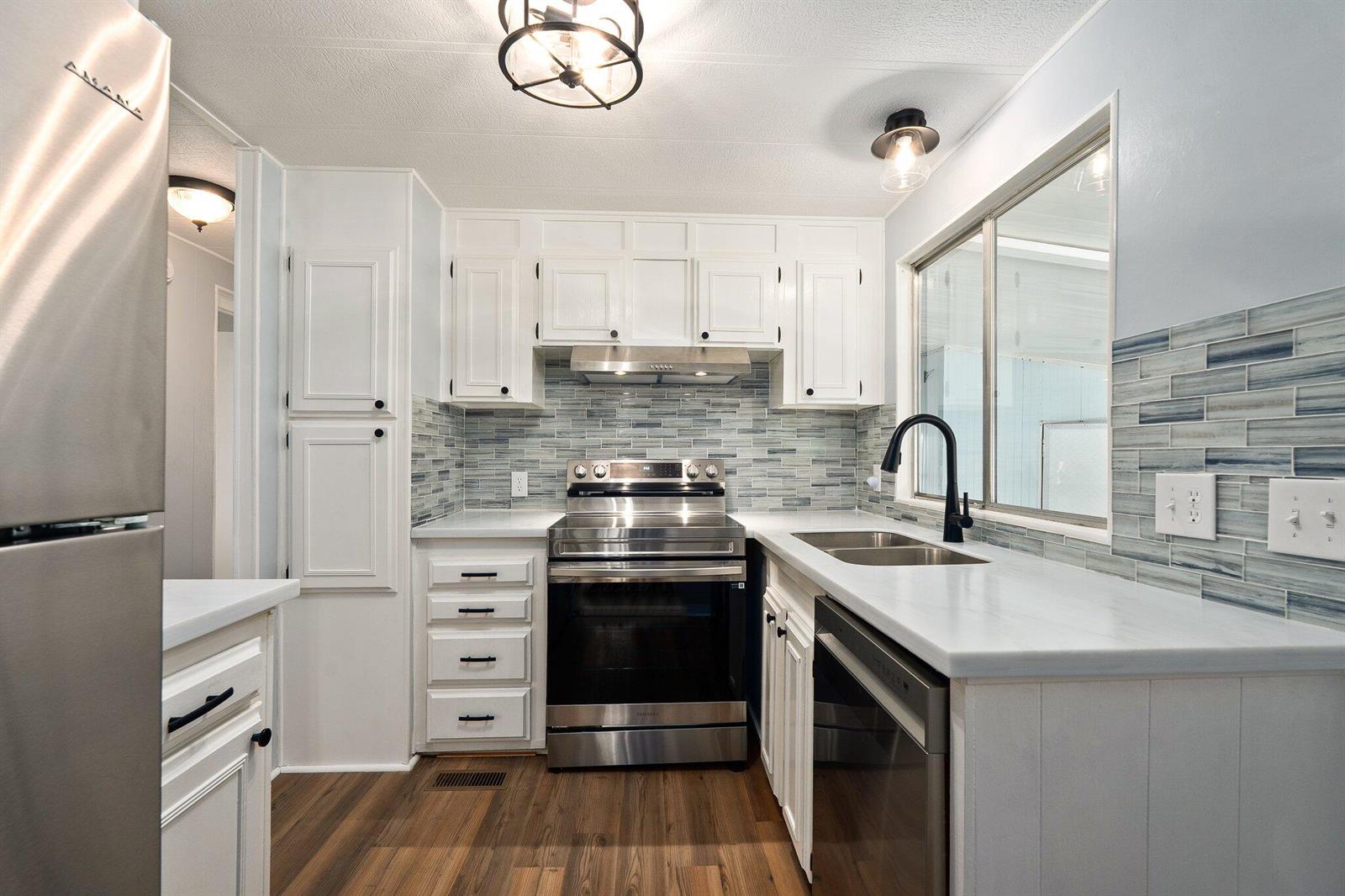 A kitchen features white cabinets, stainless steel appliances, a blue tiled backsplash, and wood flooring — 4800 SE Federal Highway # 53, Stuart FL 34997, STUART, FL
