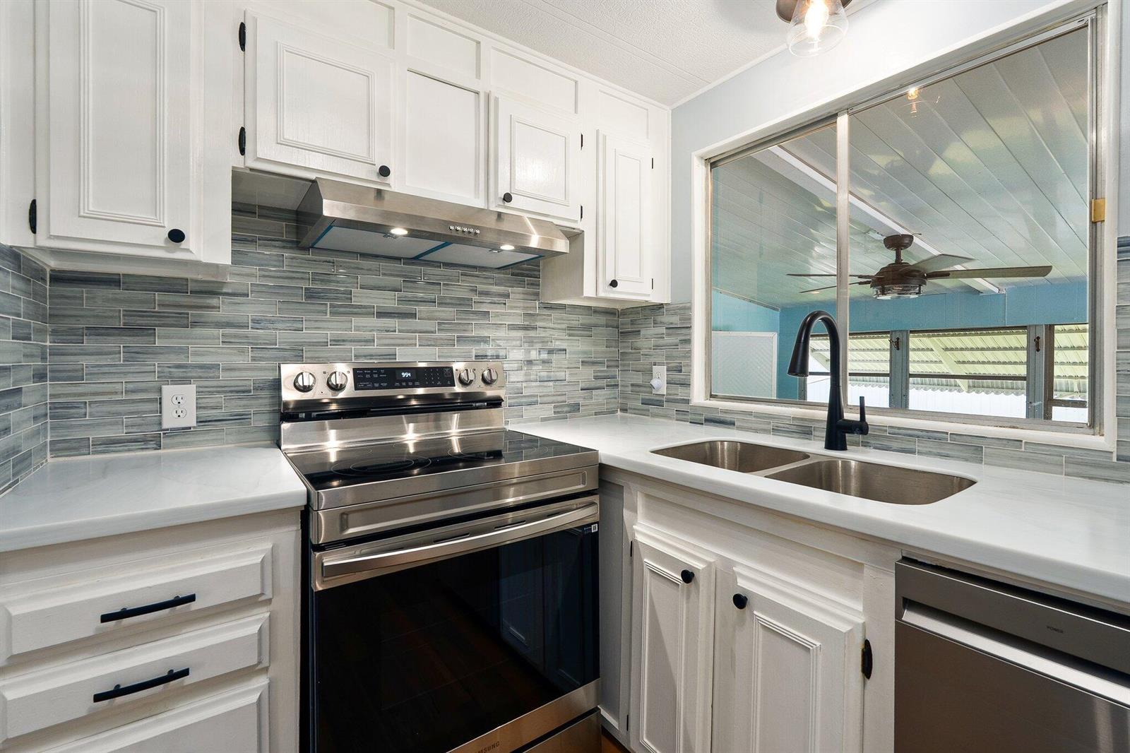 A kitchen features white cabinets, stainless steel appliances, a blue-grey tile backsplash, and a window — 4800 SE Federal Highway # 53, Stuart FL 34997, STUART, FL