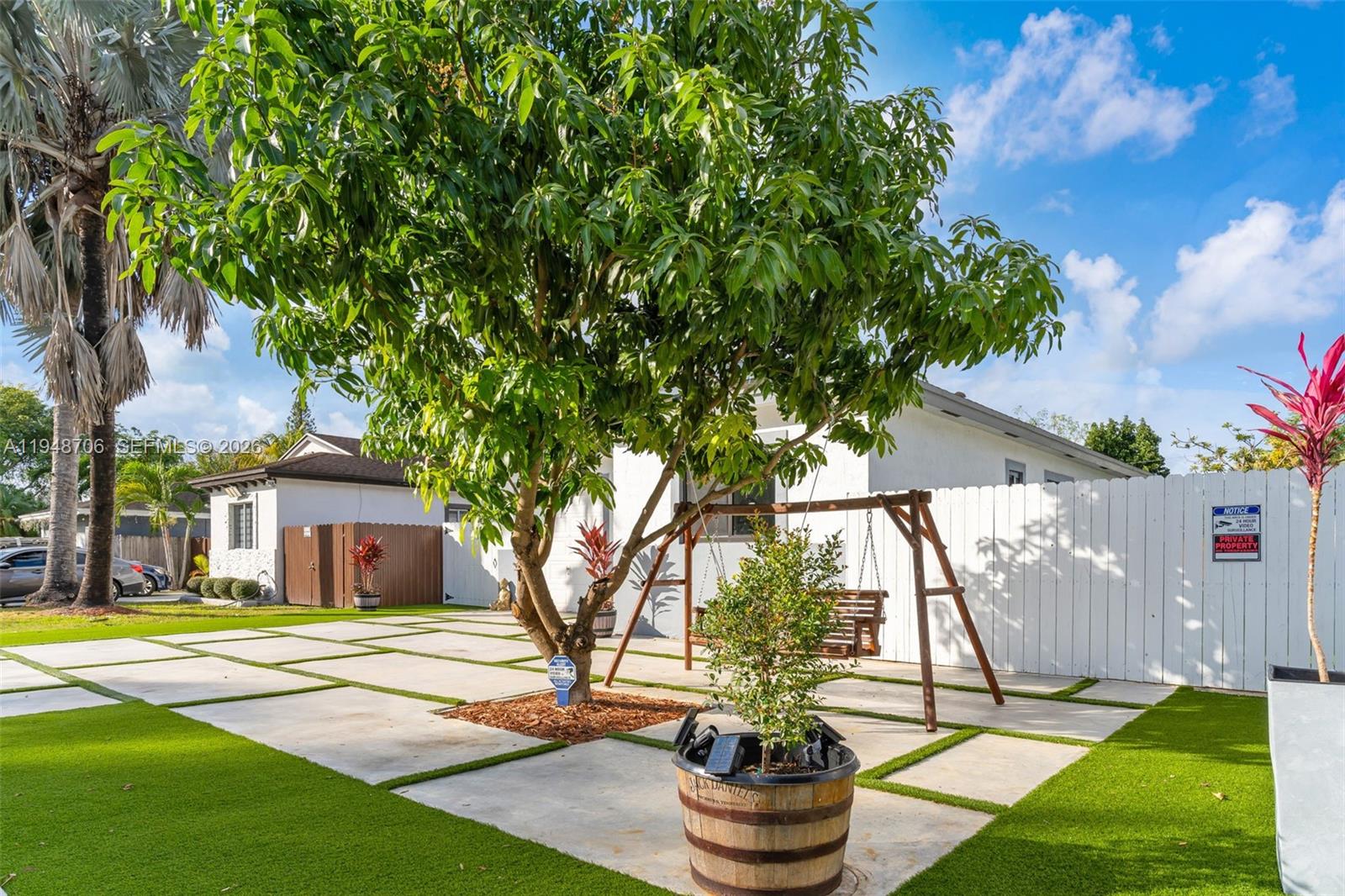 A backyard features a large tree, a wooden swing set, and concrete pavers with grass — 407 NW 9th Ct, Homestead FL 33030, HOMESTEAD, FL