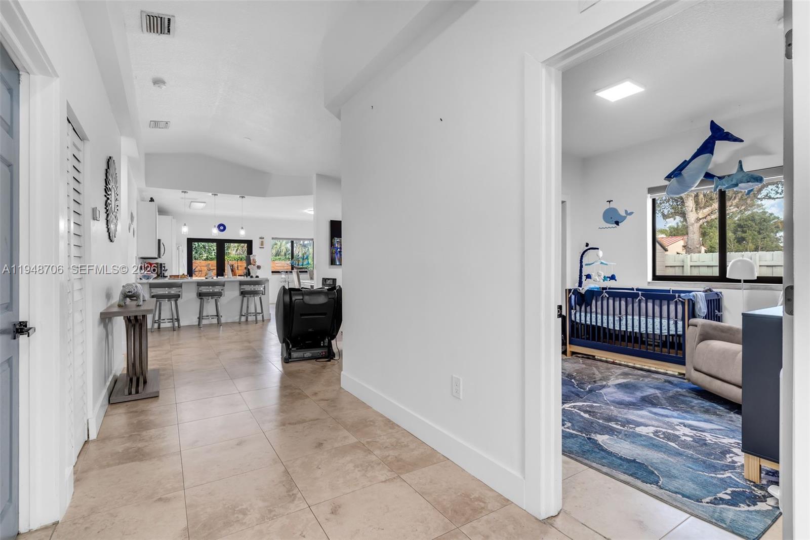 A hallway leads to a kitchen with a breakfast bar and a nursery with a crib — 407 NW 9th Ct, Homestead FL 33030, HOMESTEAD, FL
