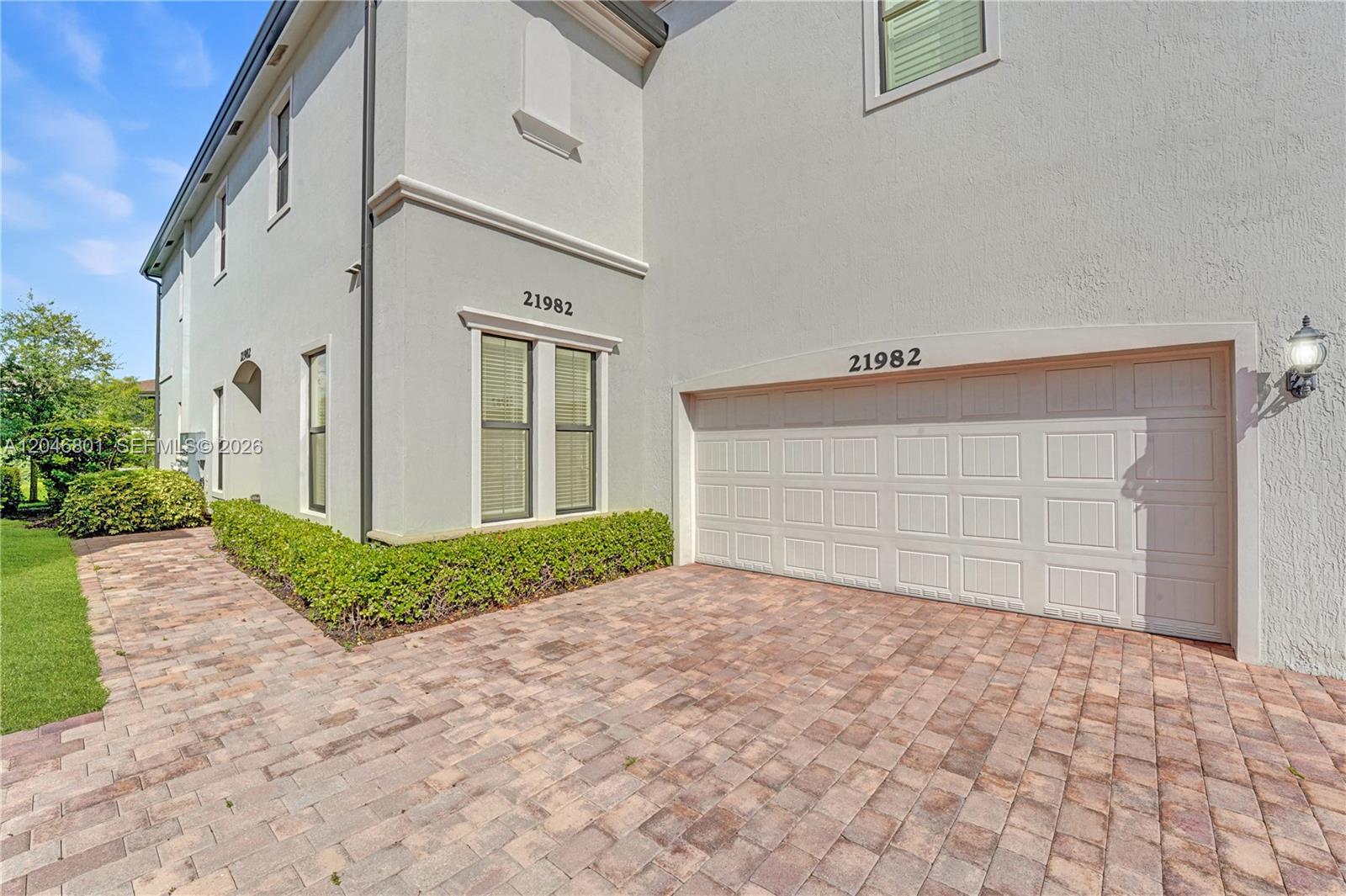 A two-story house exterior features a paved driveway, a white garage door, and landscaping — 21982 Canadensis Cir # 101, Boca Raton FL 33428, BOCA RATON, FL