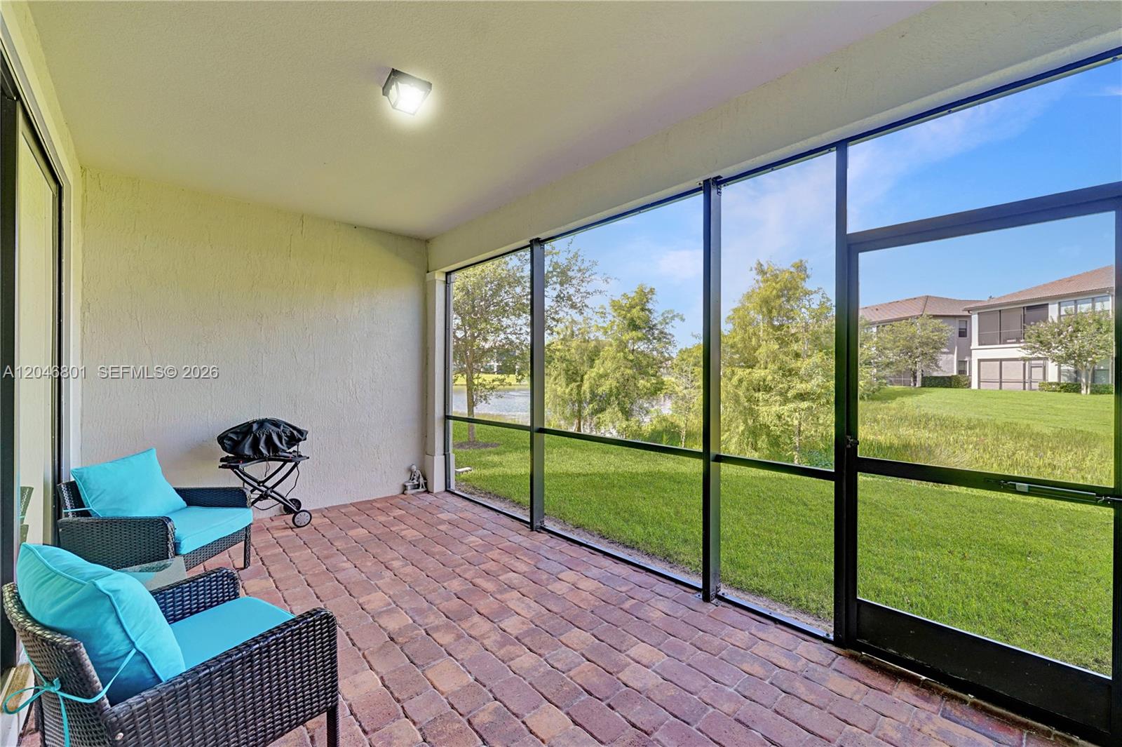 A screened-in patio features brick pavers, two wicker chairs with blue cushions, and lake views — 21982 Canadensis Cir # 101, Boca Raton FL 33428, BOCA RATON, FL