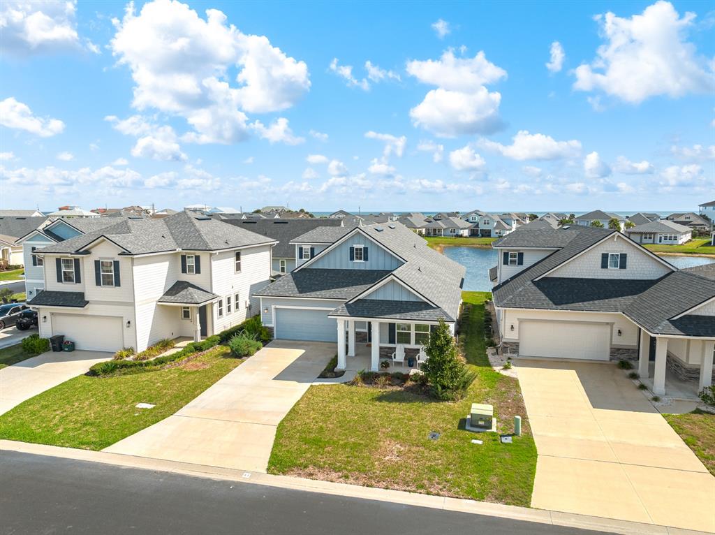 An aerial view shows three suburban houses with driveways and lawns near a small pond — 41 LOS LAGOS BOULEVARD, PALM COAST, FL