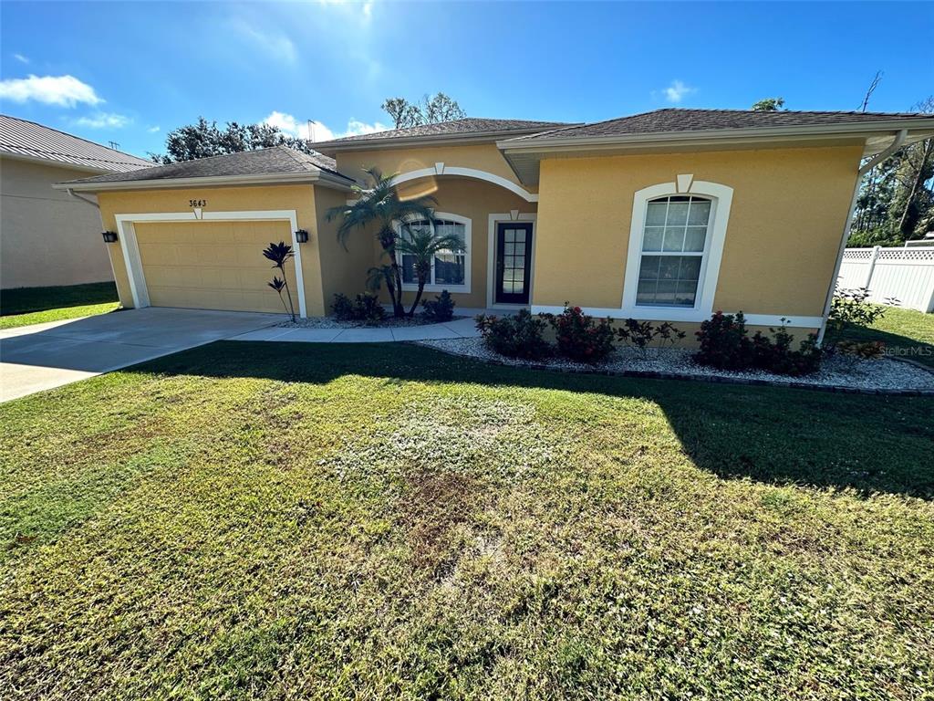 A single-story yellow house with a two-car garage and a front yard under blue skies — 3643 SPINNER AVENUE, NORTH PORT, FL
