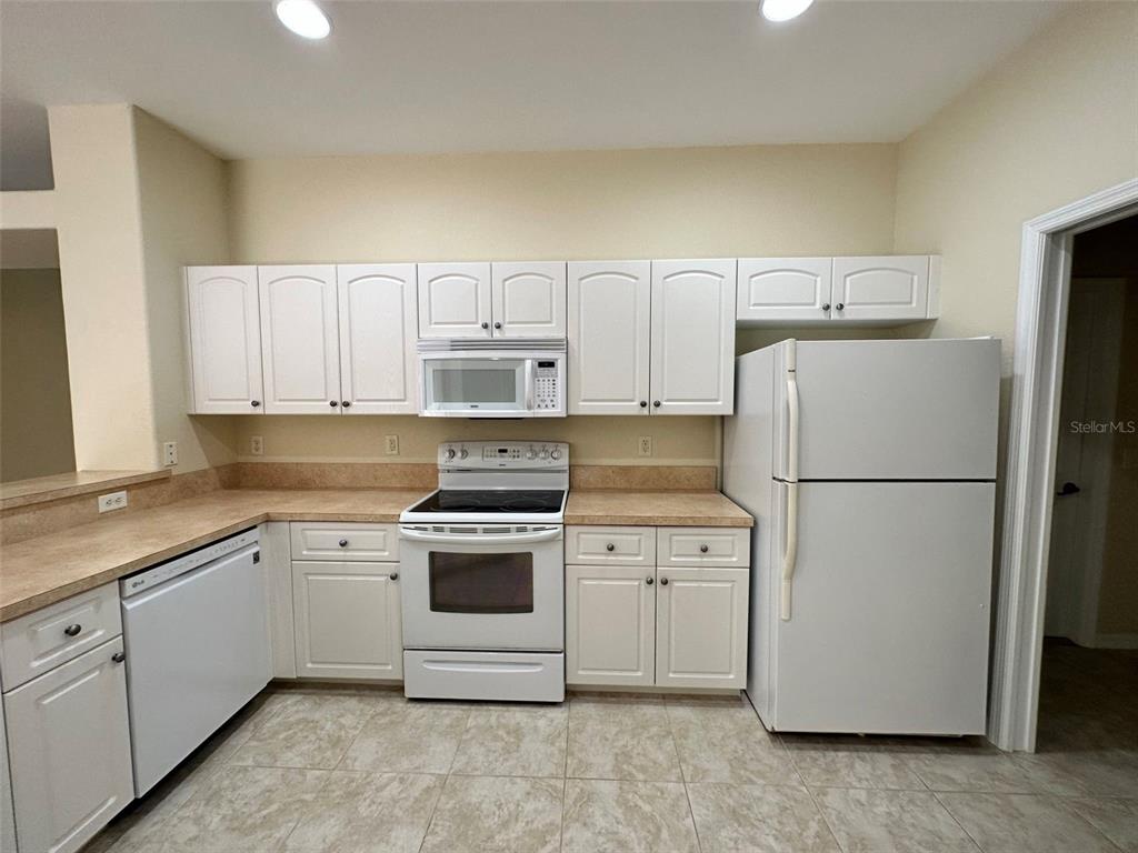 A kitchen features white cabinets, white appliances, and tan laminate countertops with tile flooring — 3643 SPINNER AVENUE, NORTH PORT, FL