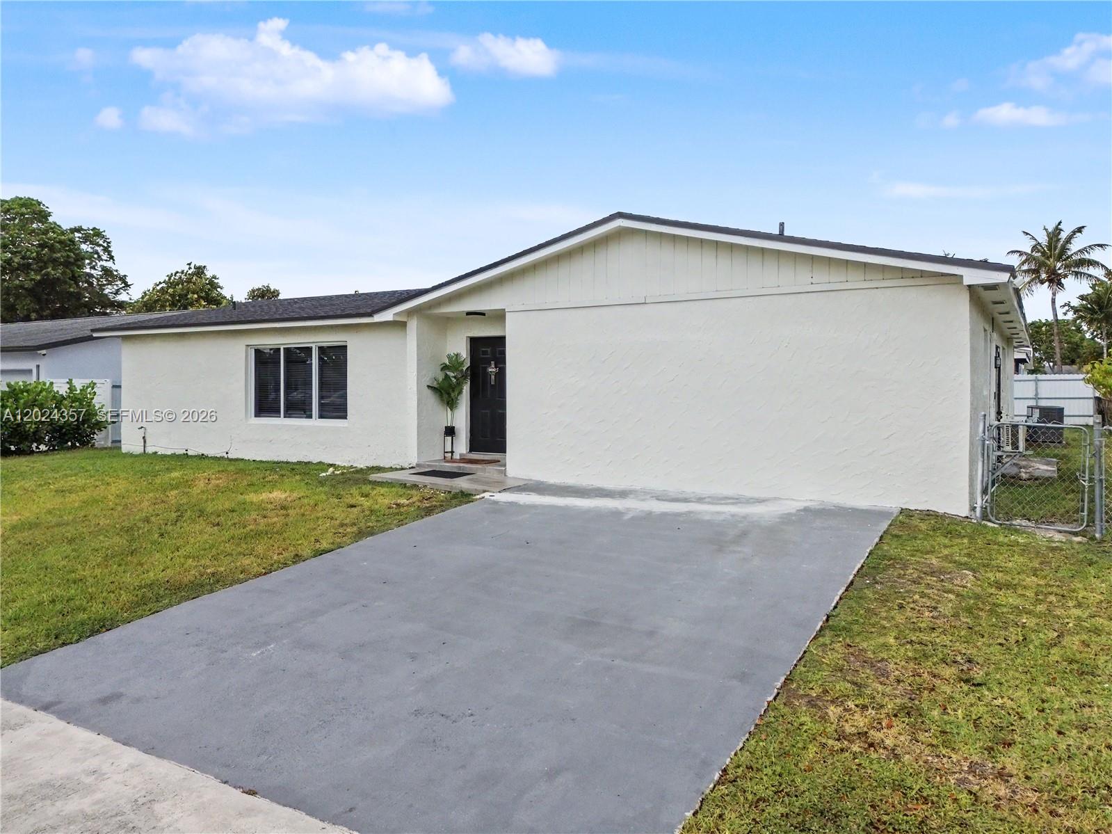 A single-story white house features a dark front door and a concrete driveway — 16912 SW 107th Pl, Miami FL 33157, MIAMI, FL