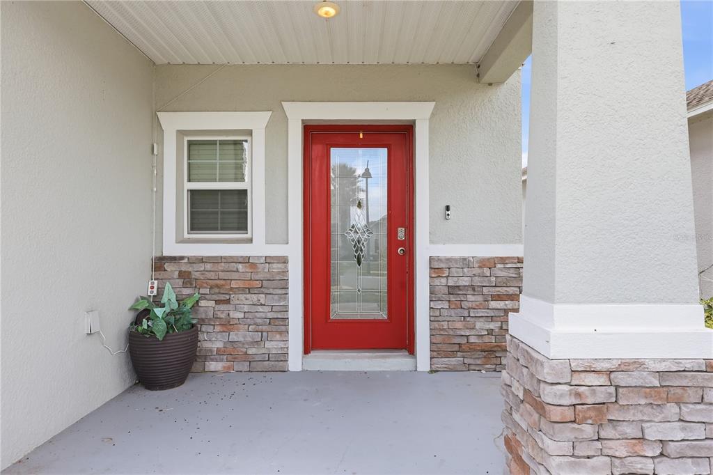 A red front door with a glass insert sits on a porch with stone accents — 850 BOCAVISTA COURT, DAVENPORT, FL