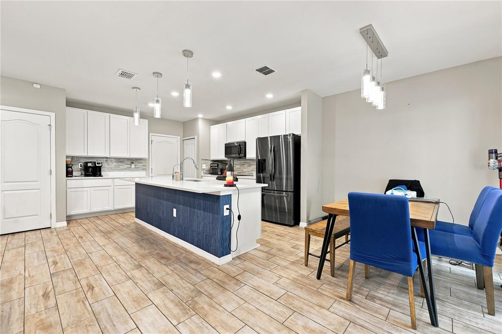 A kitchen features white cabinetry, a blue-paneled island, stainless steel appliances, and wood-look tile flooring — 850 BOCAVISTA COURT, DAVENPORT, FL