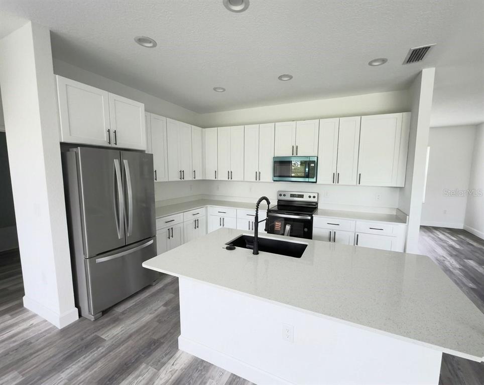 A modern kitchen features white cabinets, stainless steel appliances, a kitchen island, and gray flooring — 14683 INGRAHAM BOULEVARD, PORT CHARLOTTE, FL