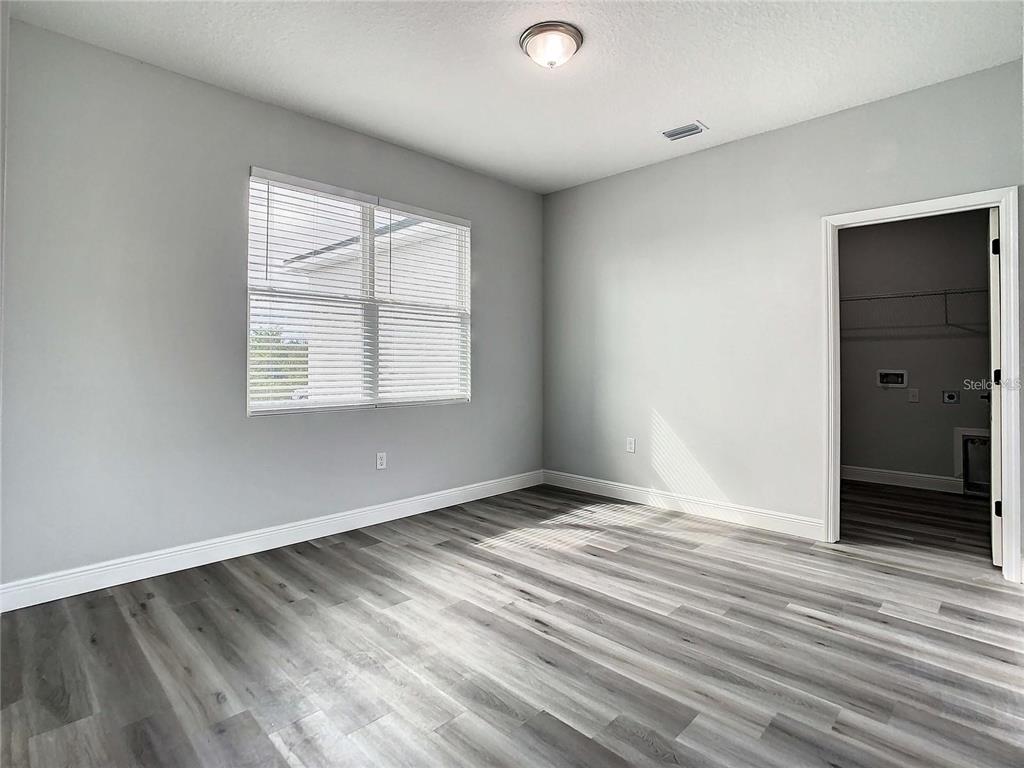 An empty room features gray walls, wood-look flooring, a window with blinds, and a doorway — 14683 INGRAHAM BOULEVARD, PORT CHARLOTTE, FL