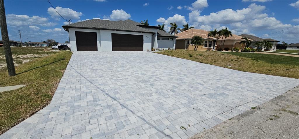 A modern single-story house features a large paver driveway and a three-car garage — 3413 NW 18TH STREET, CAPE CORAL, FL