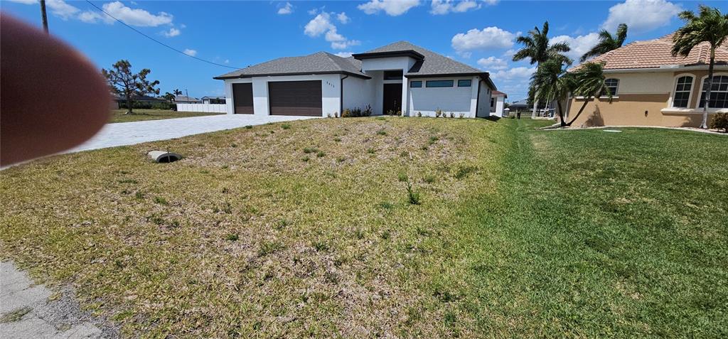 A modern single-story house with a white exterior and a brown garage sits on a lot — 3413 NW 18TH STREET, CAPE CORAL, FL