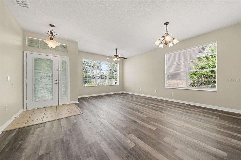 An empty living room features gray wood-look flooring, a ceiling fan, and two light fixtures — 278 VENETIAN BAY CIRCLE, SANFORD, FL