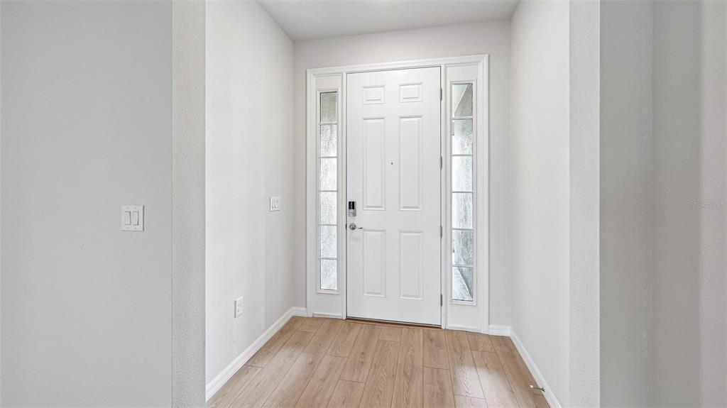 An entryway features a white front door with sidelights and light wood-look flooring — 1517 LOVE GRASS TERRACE, PARRISH, FL