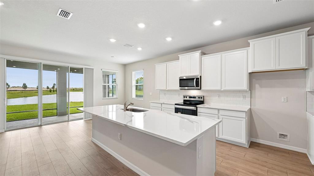 A modern kitchen features white cabinets, a quartz-topped island, and sliding doors overlooking a pond — 1517 LOVE GRASS TERRACE, PARRISH, FL