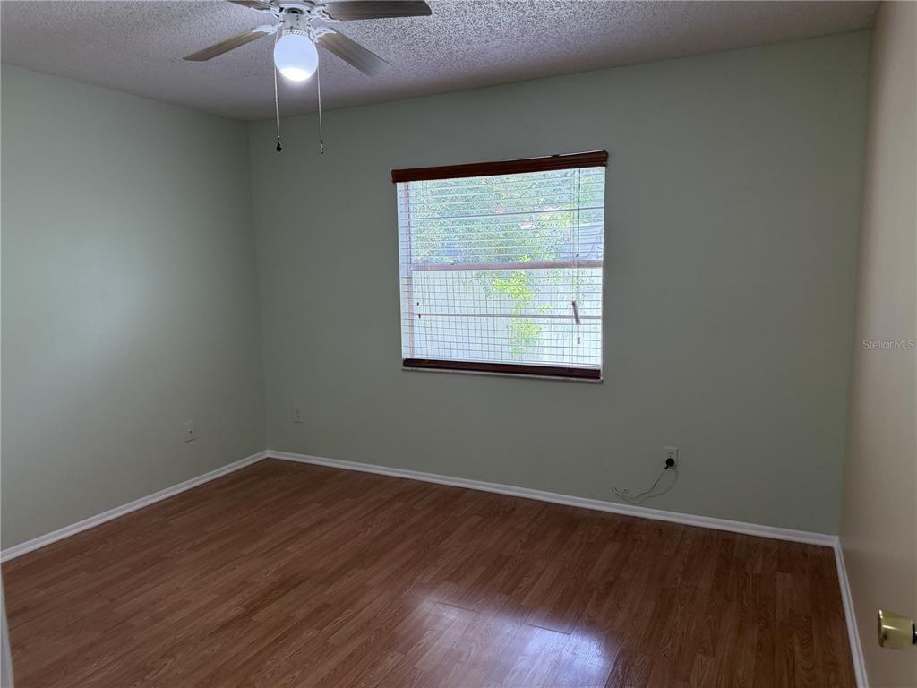 An empty bedroom features light green walls, wood-look flooring, a ceiling fan, and a window — 1316 MILL CREEK PLACE, KISSIMMEE, FL
