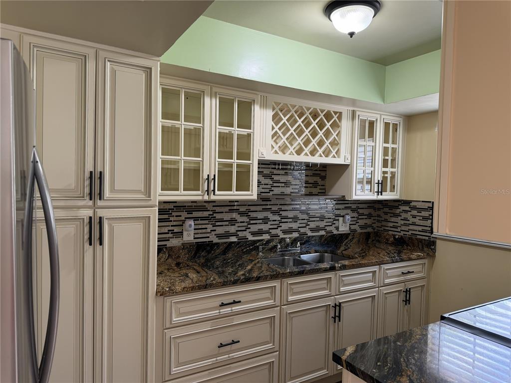 A kitchen features cream-colored cabinets, granite countertops, a mosaic tile backsplash, and a wine rack — 1316 MILL CREEK PLACE, KISSIMMEE, FL