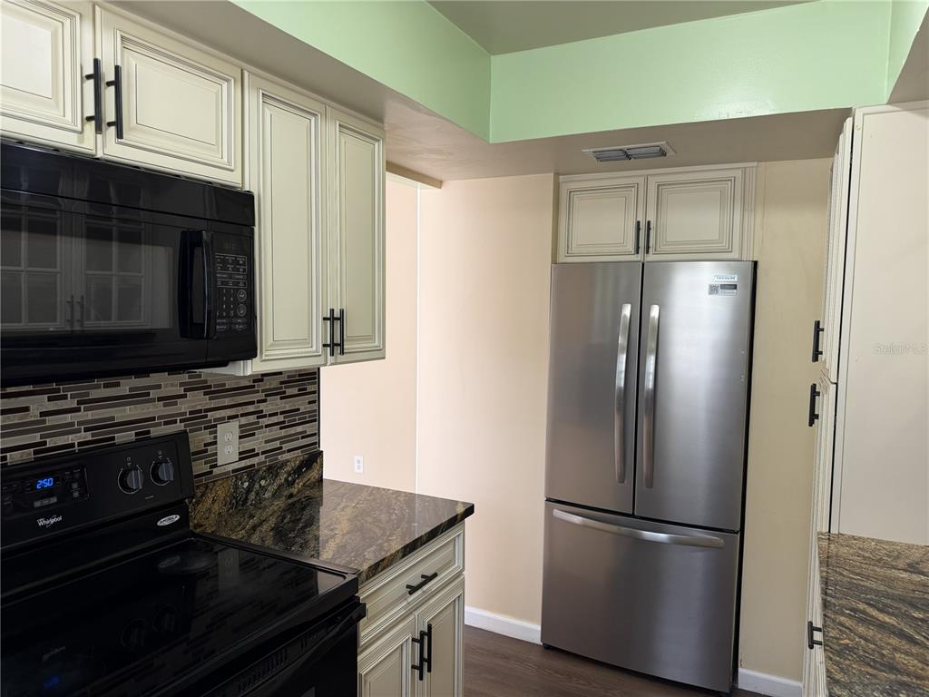 A kitchen features white cabinets, stainless steel appliances, and dark granite countertops with a tiled backsplash — 1316 MILL CREEK PLACE, KISSIMMEE, FL