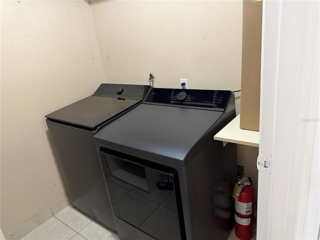 A laundry room features a dark gray washer and dryer set next to a fire extinguisher — 1316 MILL CREEK PLACE, KISSIMMEE, FL