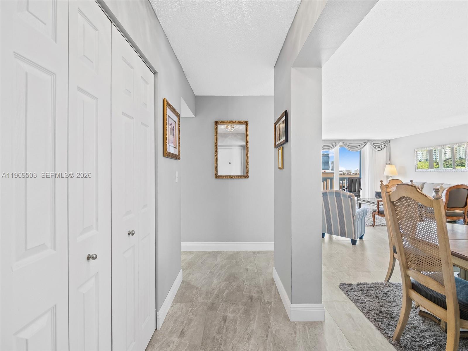A hallway with white bi-fold doors leads into a living and dining area with tile flooring — 401 NE 14th Ave # 808, Hallandale Beach FL 33009, HALLANDALE BEACH, FL