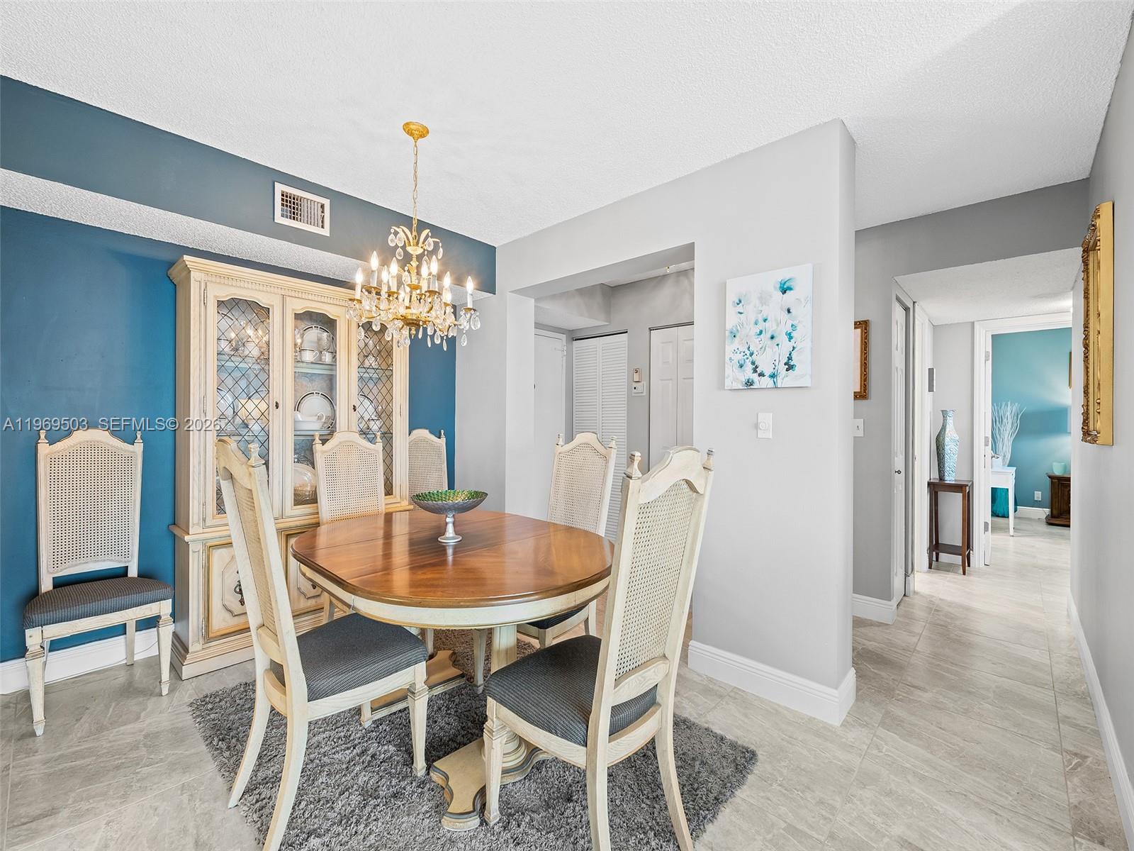 A dining room features a round wooden table, cane-back chairs, and a crystal chandelier — 401 NE 14th Ave # 808, Hallandale Beach FL 33009, HALLANDALE BEACH, FL