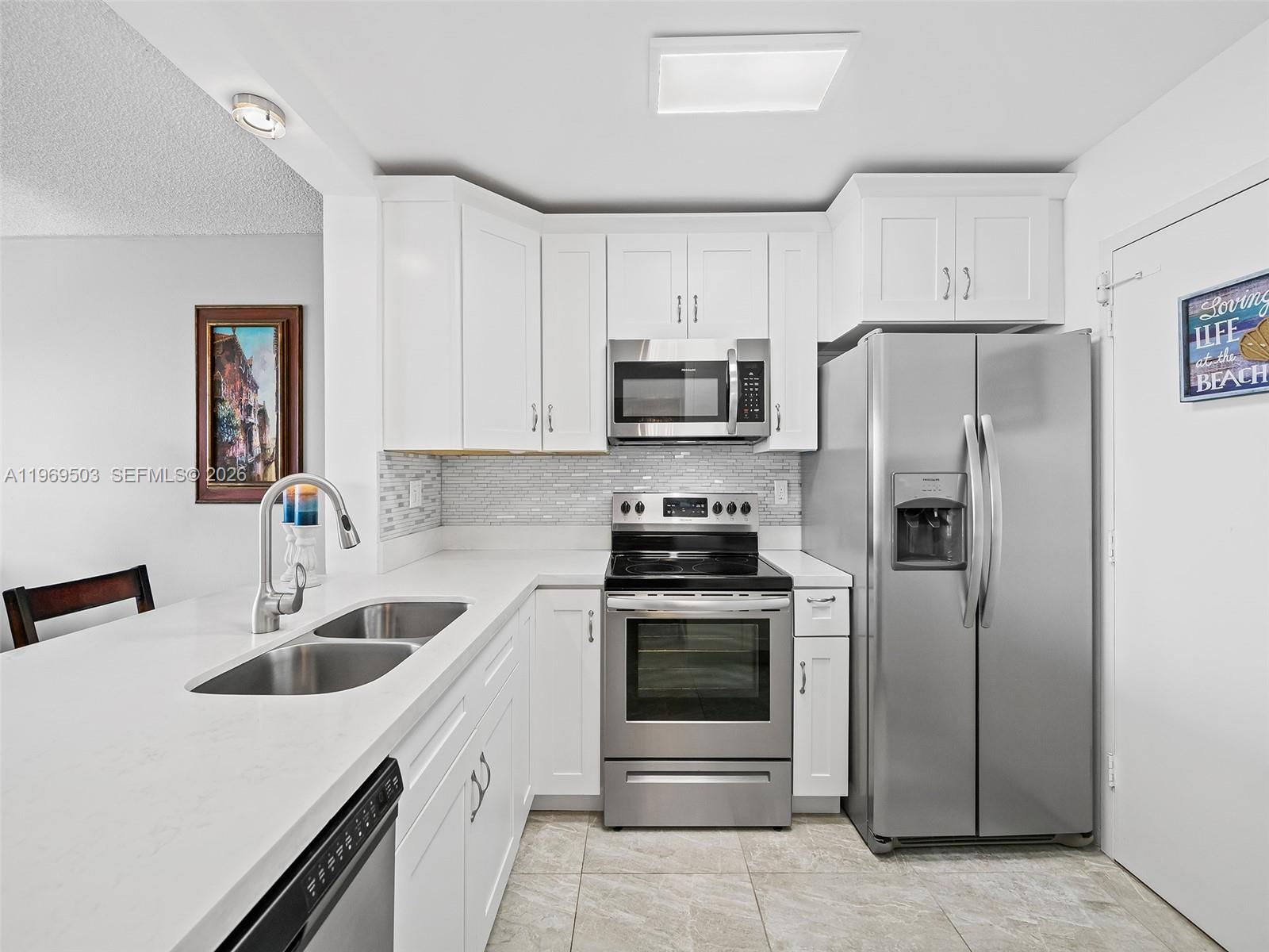 A kitchen features white cabinets, stainless steel appliances, a tiled backsplash, and a quartz countertop — 401 NE 14th Ave # 808, Hallandale Beach FL 33009, HALLANDALE BEACH, FL