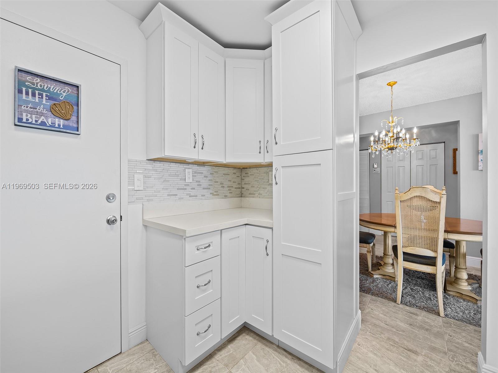 A white kitchen corner cabinet unit features a tiled backsplash and a nearby dining area — 401 NE 14th Ave # 808, Hallandale Beach FL 33009, HALLANDALE BEACH, FL