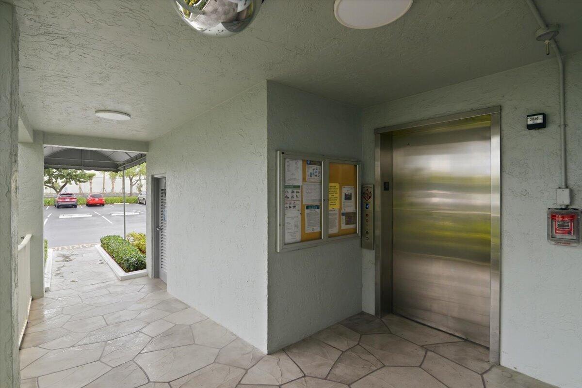 An elevator lobby with a bulletin board and a view of an outdoor parking lot — 2220 N Cypress Bend Drive # 410, Pompano Beach FL 33069, POMPANO BEACH, FL