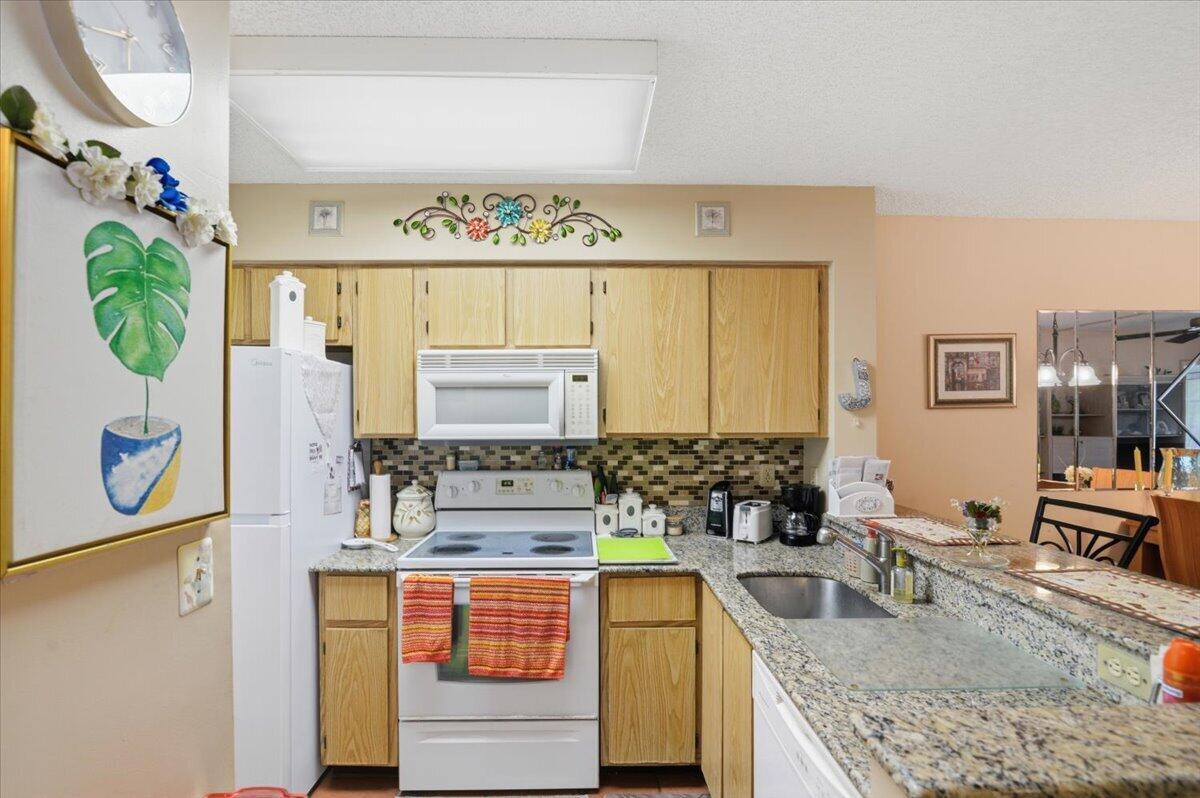 A kitchen features light wood cabinets, granite countertops, a white appliance suite, and tile backsplash — 2220 N Cypress Bend Drive # 410, Pompano Beach FL 33069, POMPANO BEACH, FL