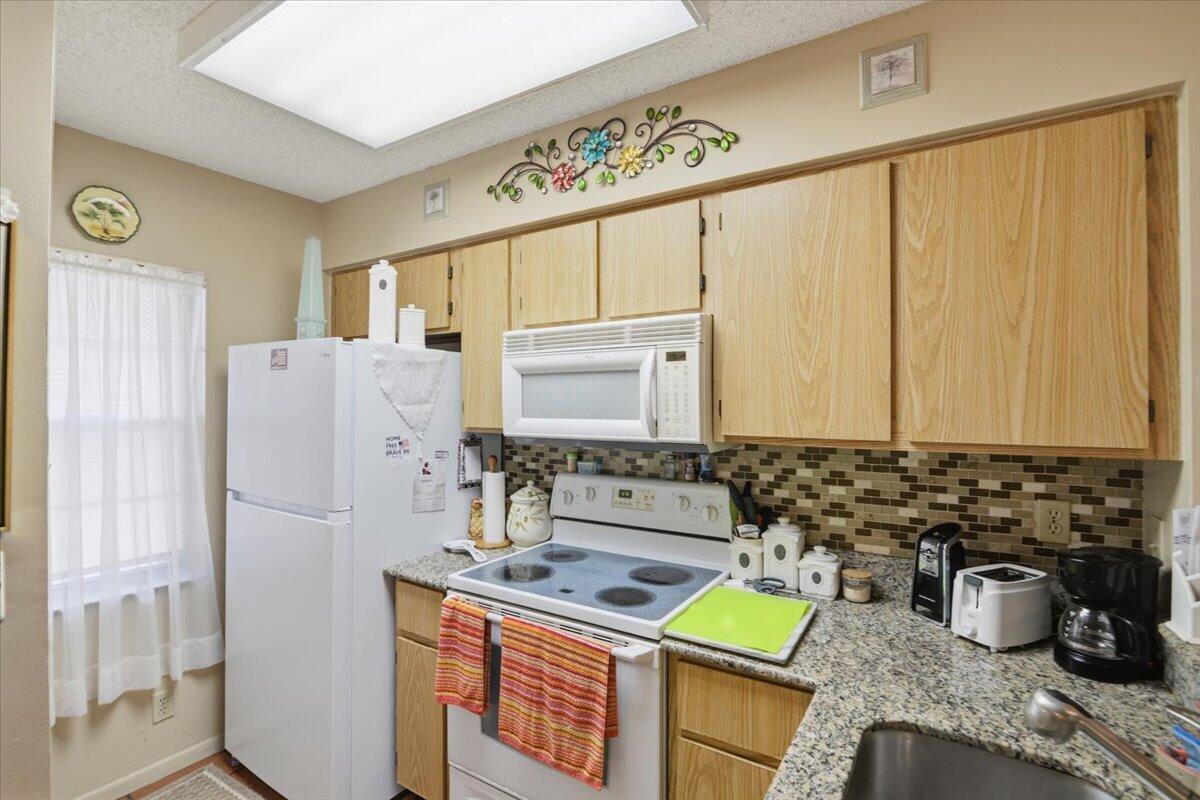 A kitchen features light wood cabinets, granite countertops, a mosaic tile backsplash, and white appliances — 2220 N Cypress Bend Drive # 410, Pompano Beach FL 33069, POMPANO BEACH, FL