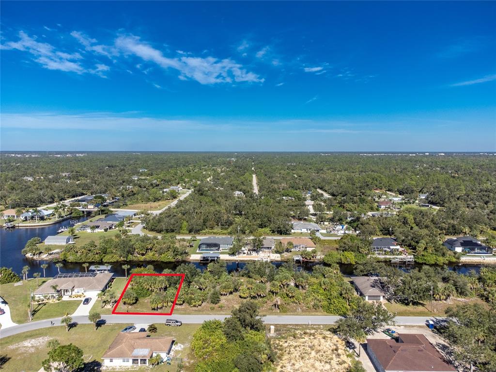 An aerial view shows a vacant, wooded residential lot outlined in red along a canal — 17324 GULFSPRAY CIRCLE, PORT CHARLOTTE, FL