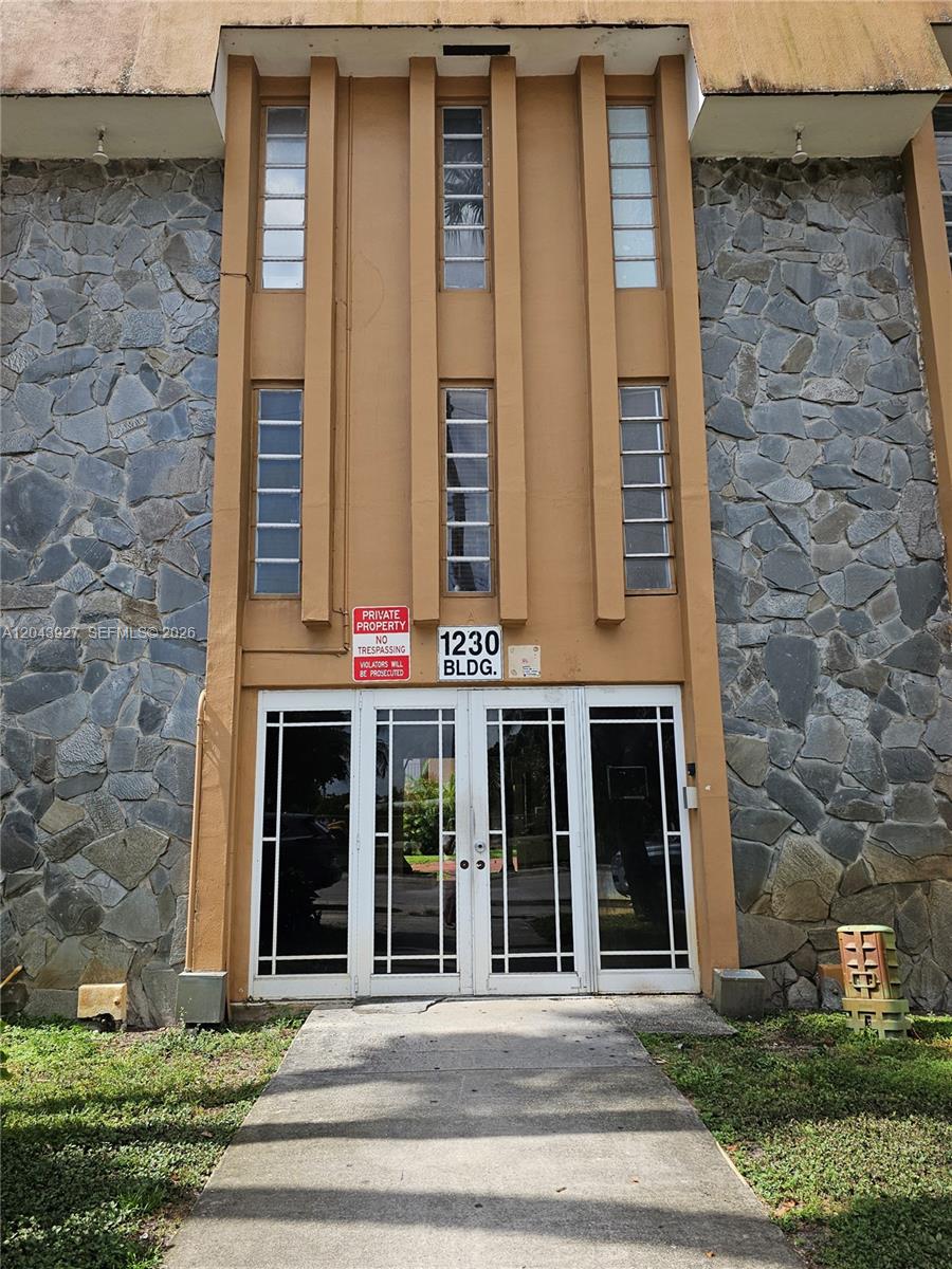 The exterior of a building features a stone facade, a central tan entryway, and glass doors — 1230 W 54th St # 218A, Hialeah FL 33012, HIALEAH, FL