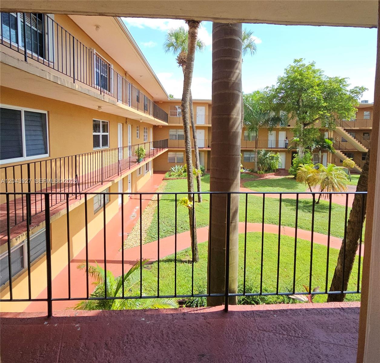 A view from a balcony overlooking a courtyard with palm trees and apartment buildings — 1230 W 54th St # 218A, Hialeah FL 33012, HIALEAH, FL