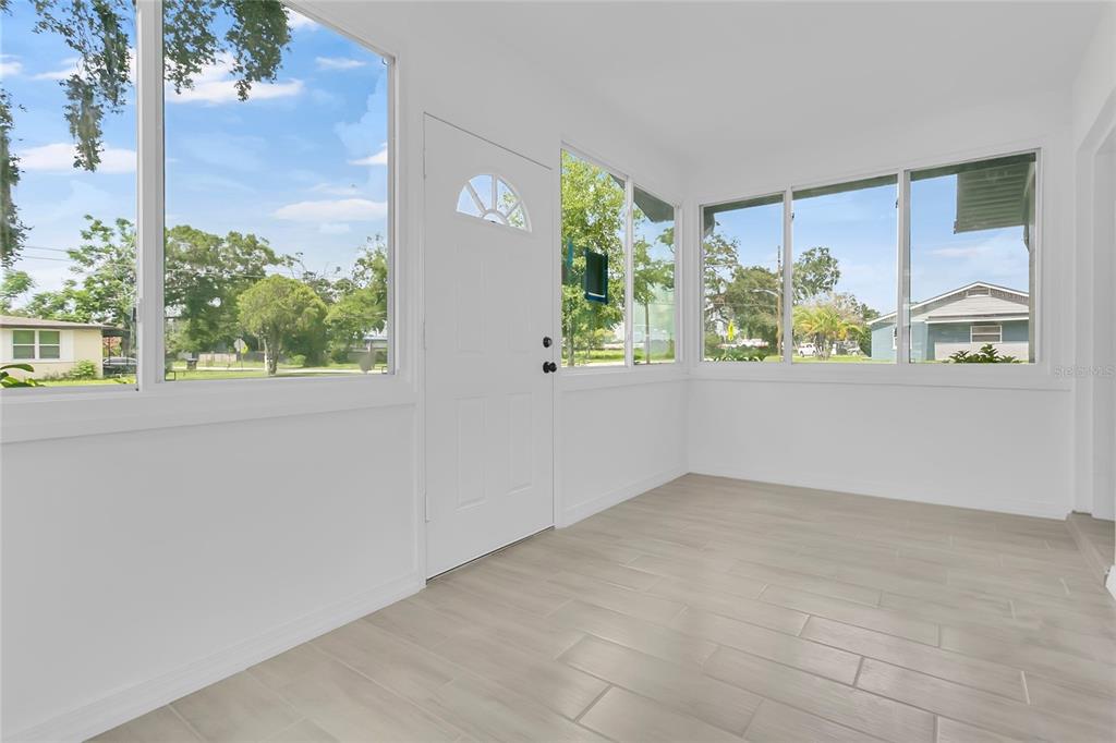 A bright sunroom features white walls, light-colored tile flooring, and large windows overlooking a neighborhood — 3504 S NASHVILLE AVENUE, ORLANDO, FL