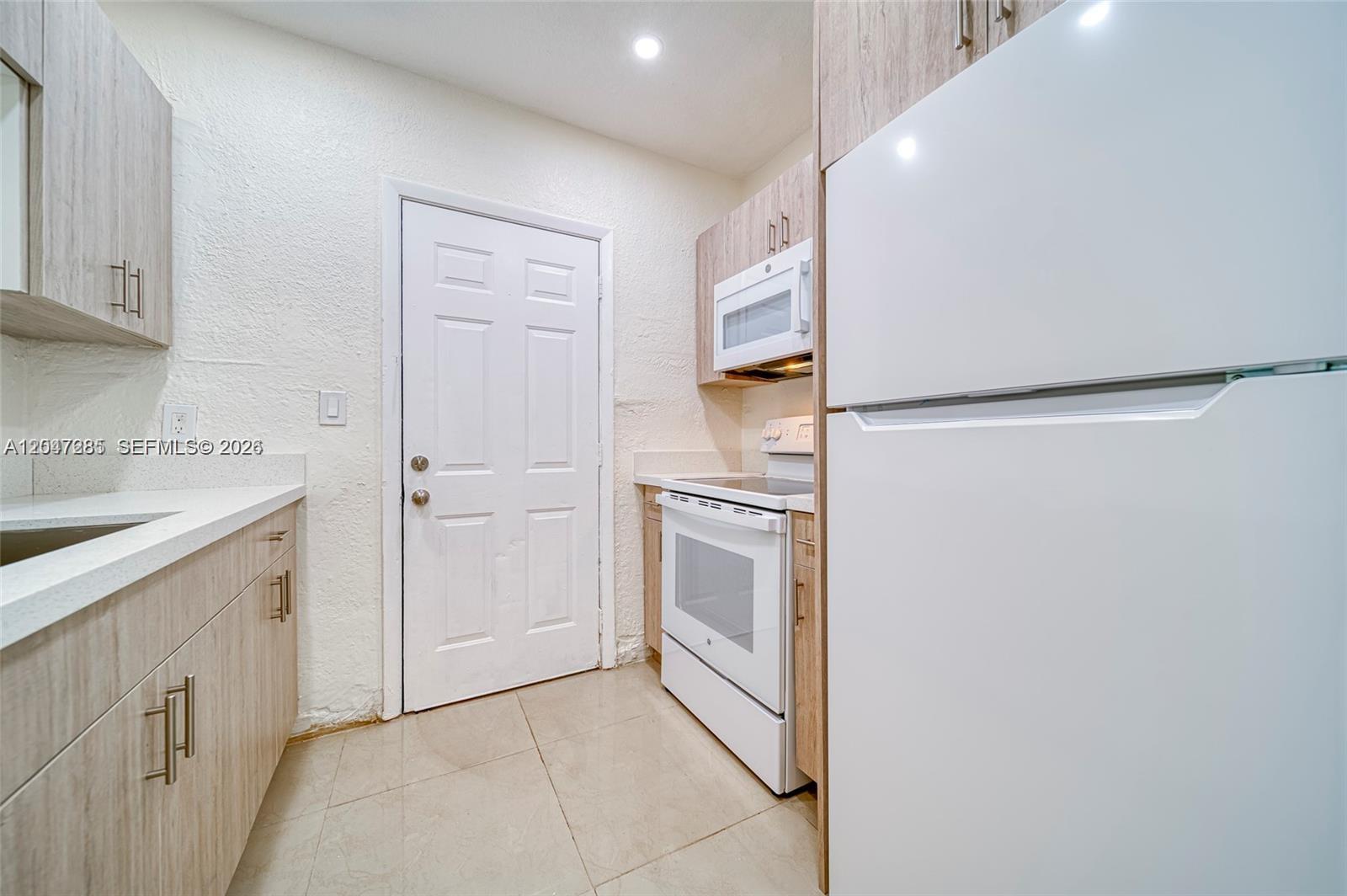 A kitchen features light wood cabinets, white appliances, a white door, and tiled flooring — 1747 NW 40th St # 1747, Miami FL 33142, MIAMI, FL