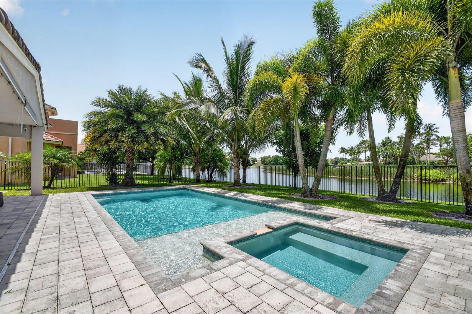 A backyard features a swimming pool and spa on a paved patio overlooking a lake — 8890 Cobblestone Point Circle, Boynton Beach FL 33472, BOYNTON BEACH, FL
